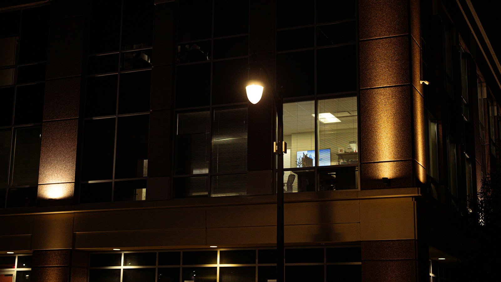 Office building at night with one lit window and a streetlight
