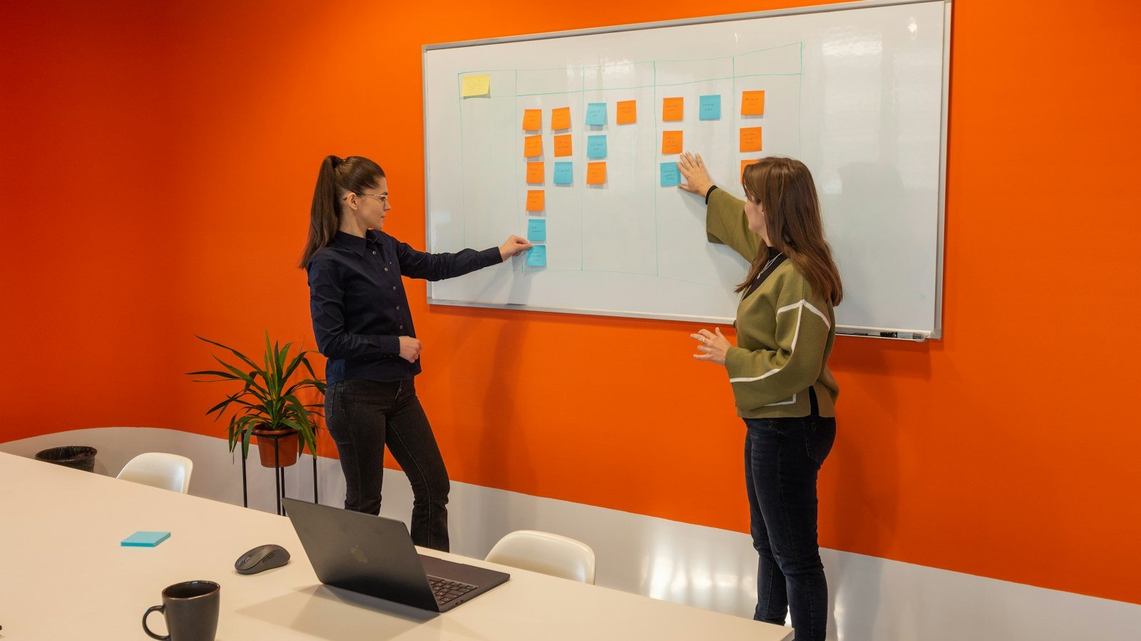 Two women arranging sticky notes on a whiteboard in a bright meeting room