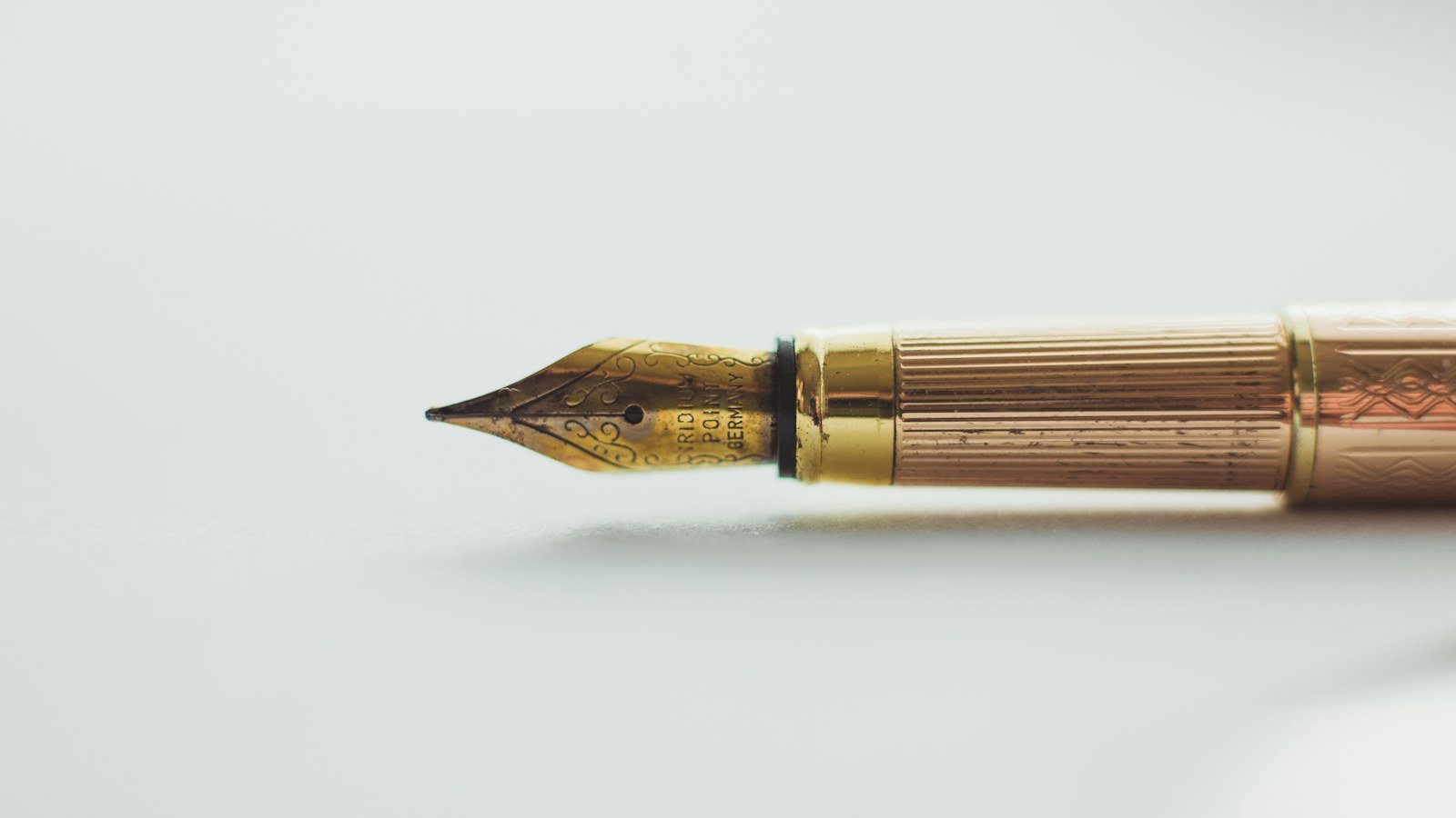 Gold fountain pen with an engraved nib lying on a white surface