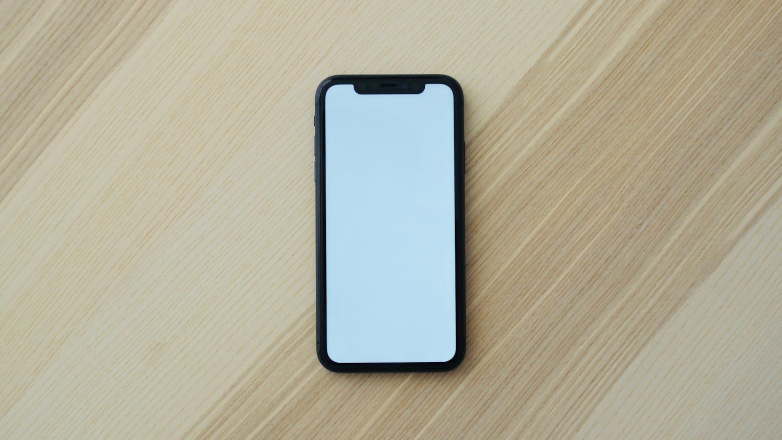 A black smartphone with a blank screen on a light wooden desk