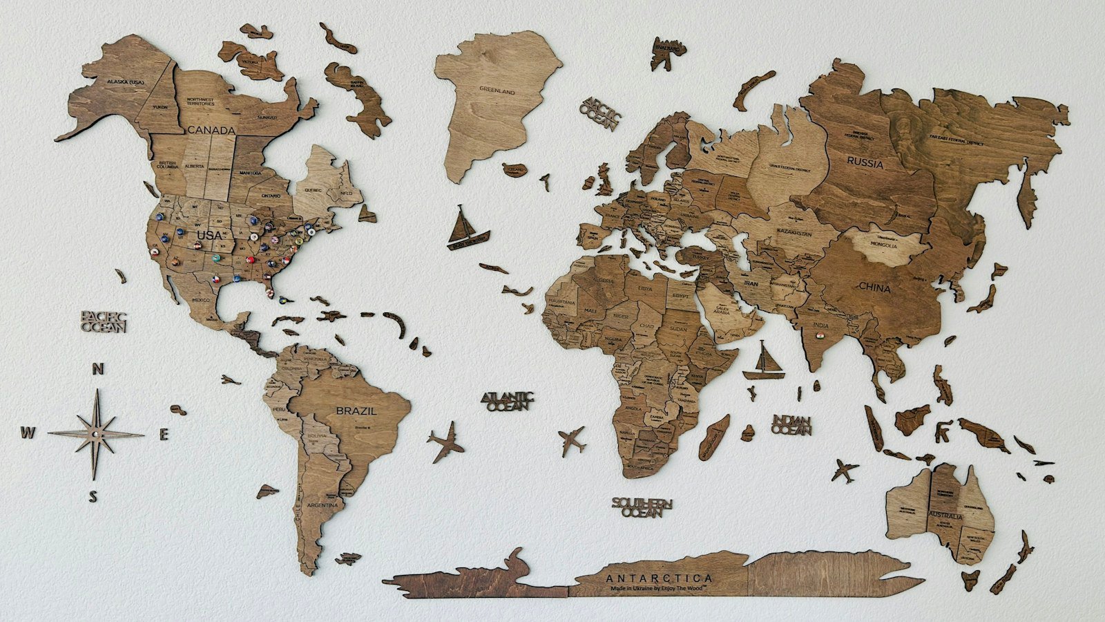 A wooden world map mounted on a plain white wall