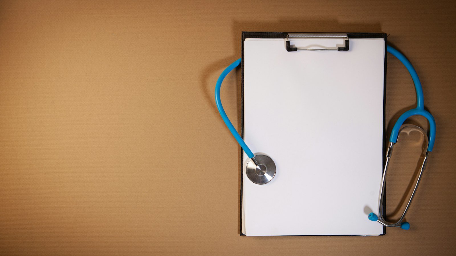 Blue stethoscope beside a blank clipboard on a brown surface