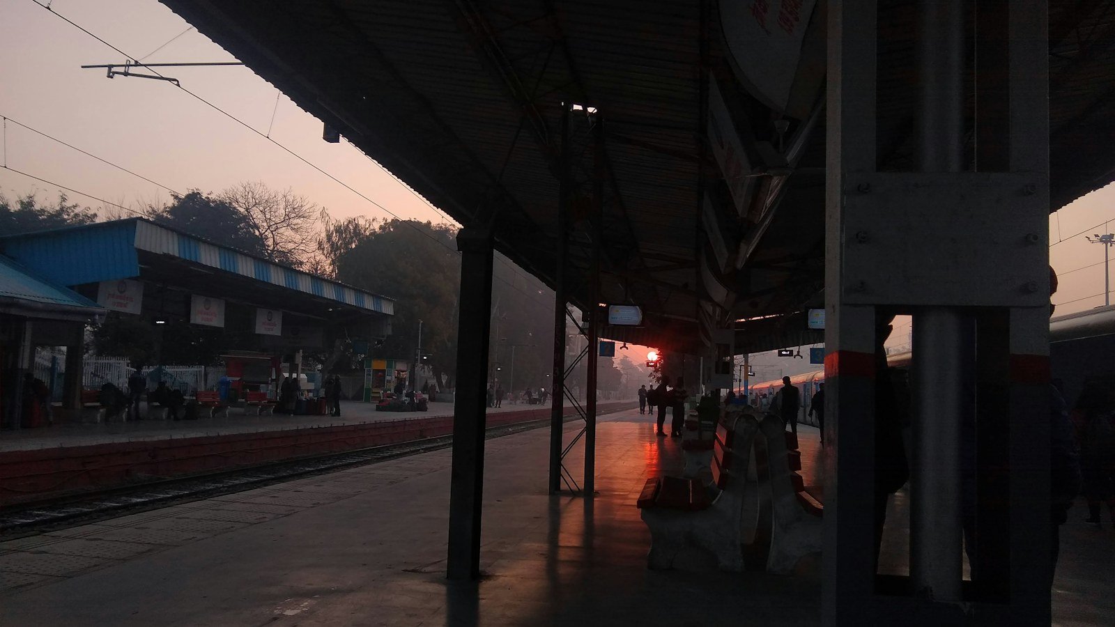 Railway station platform at sunrise with a long shed and tracks