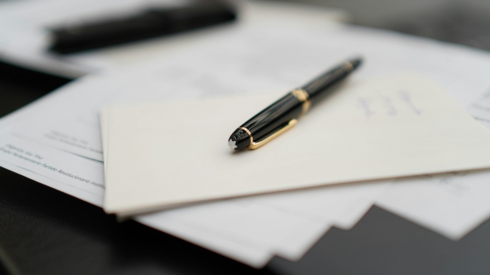 Black fountain pen resting on a stack of papers and envelopes