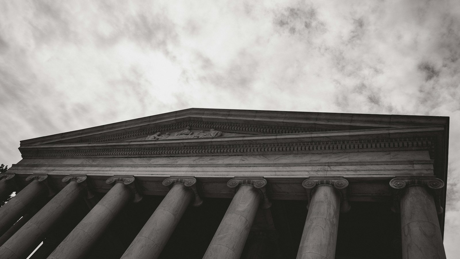 Classical stone building facade with tall columns under a cloudy sky