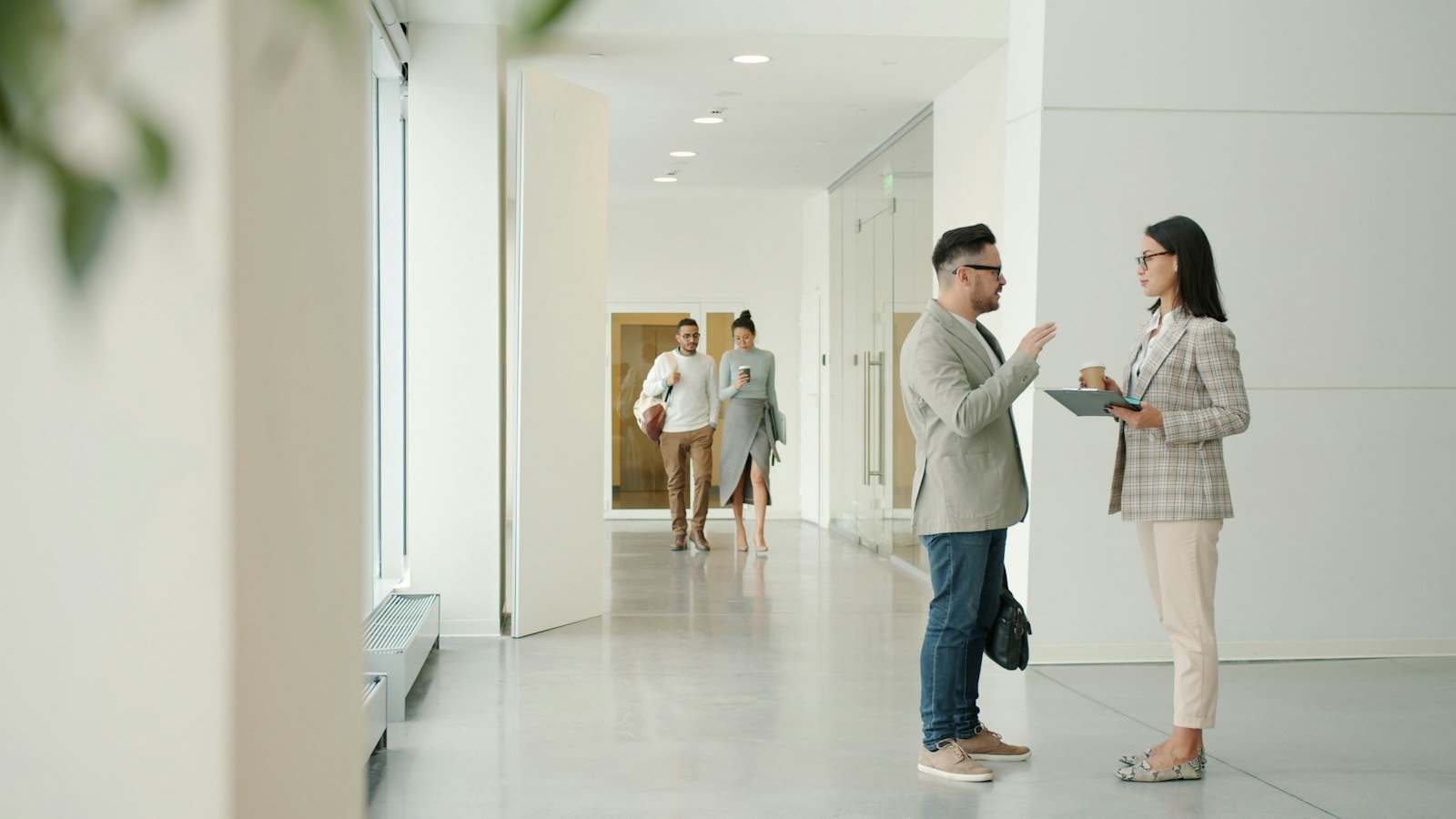 Two colleagues talking in a bright modern office hallway