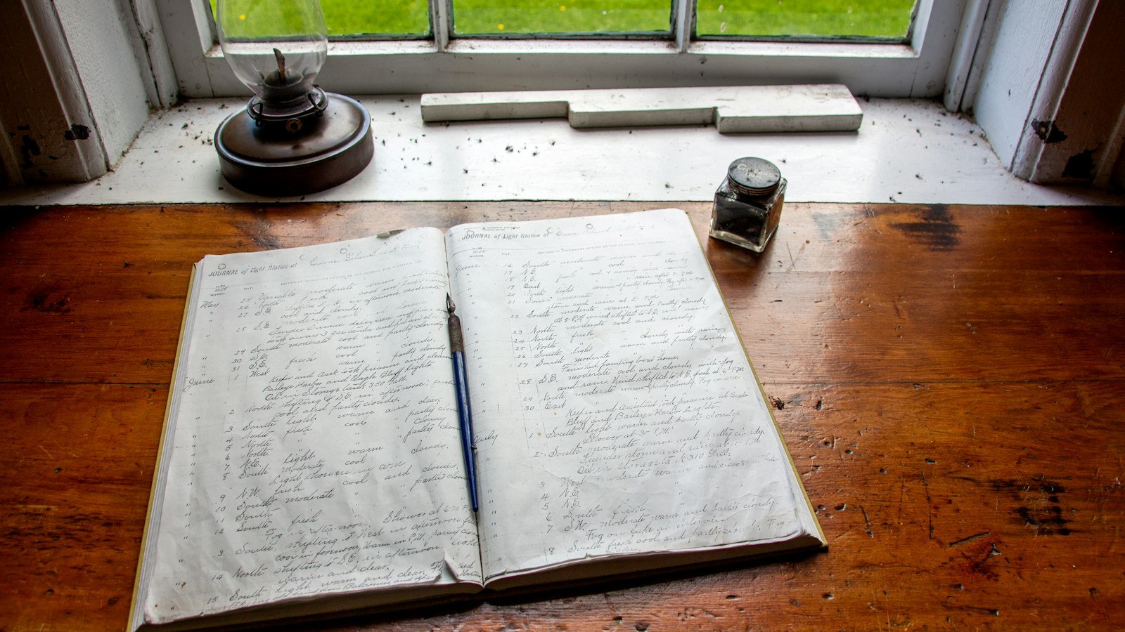 An open handwritten notebook and pen on a wooden desk by a window