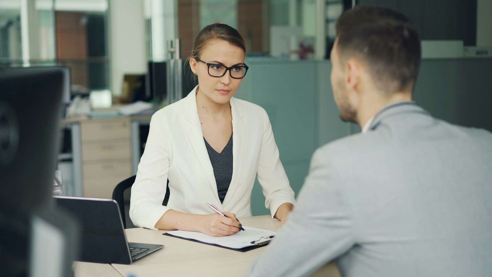 Woman in glasses interviewing a man across an office desk