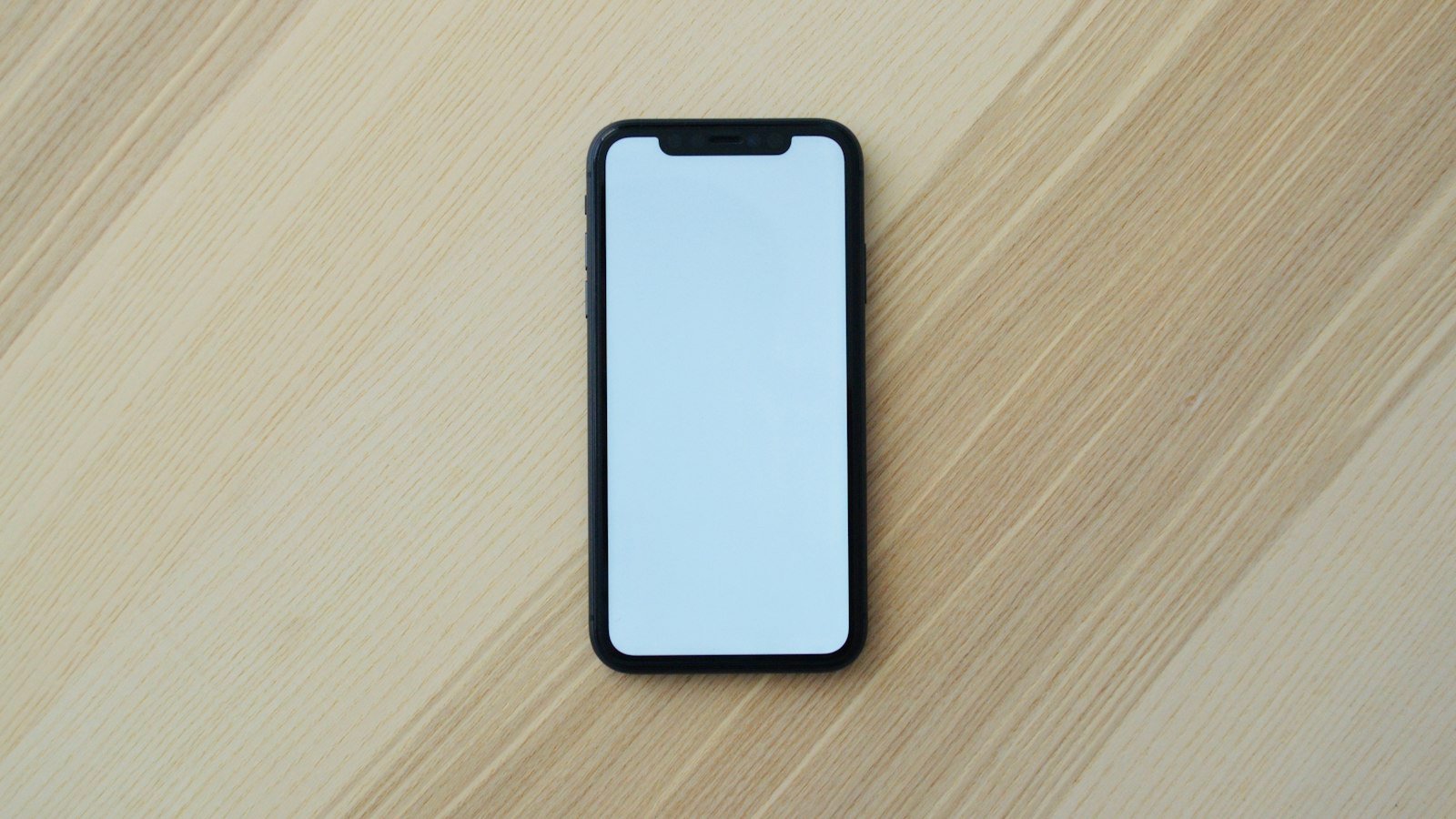 A smartphone with a blank screen lying on a pale wooden surface