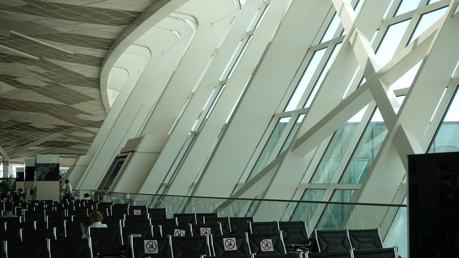 Airport terminal seating area beneath tall angled windows and a curved ceiling