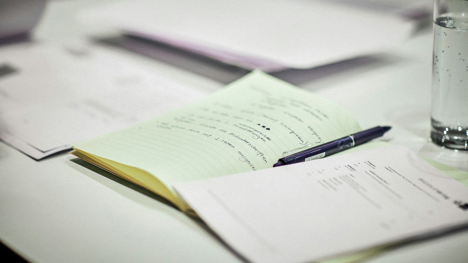 An open notepad and a pen resting on printed papers