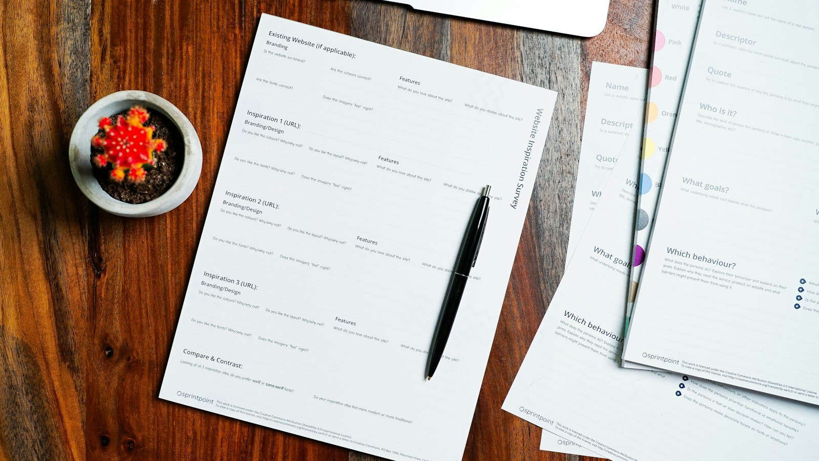 Printed papers and a pen spread across a plain wooden table