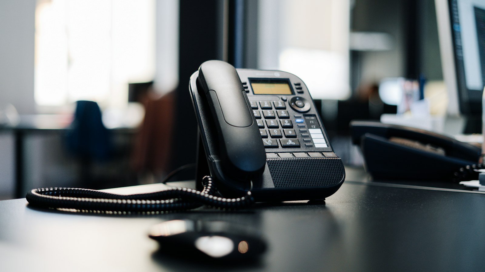 Black desk phone with coiled cord on an office desk