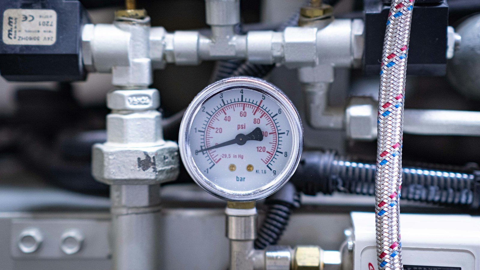 Pressure gauge fitted among metal pipes and valves on a machine