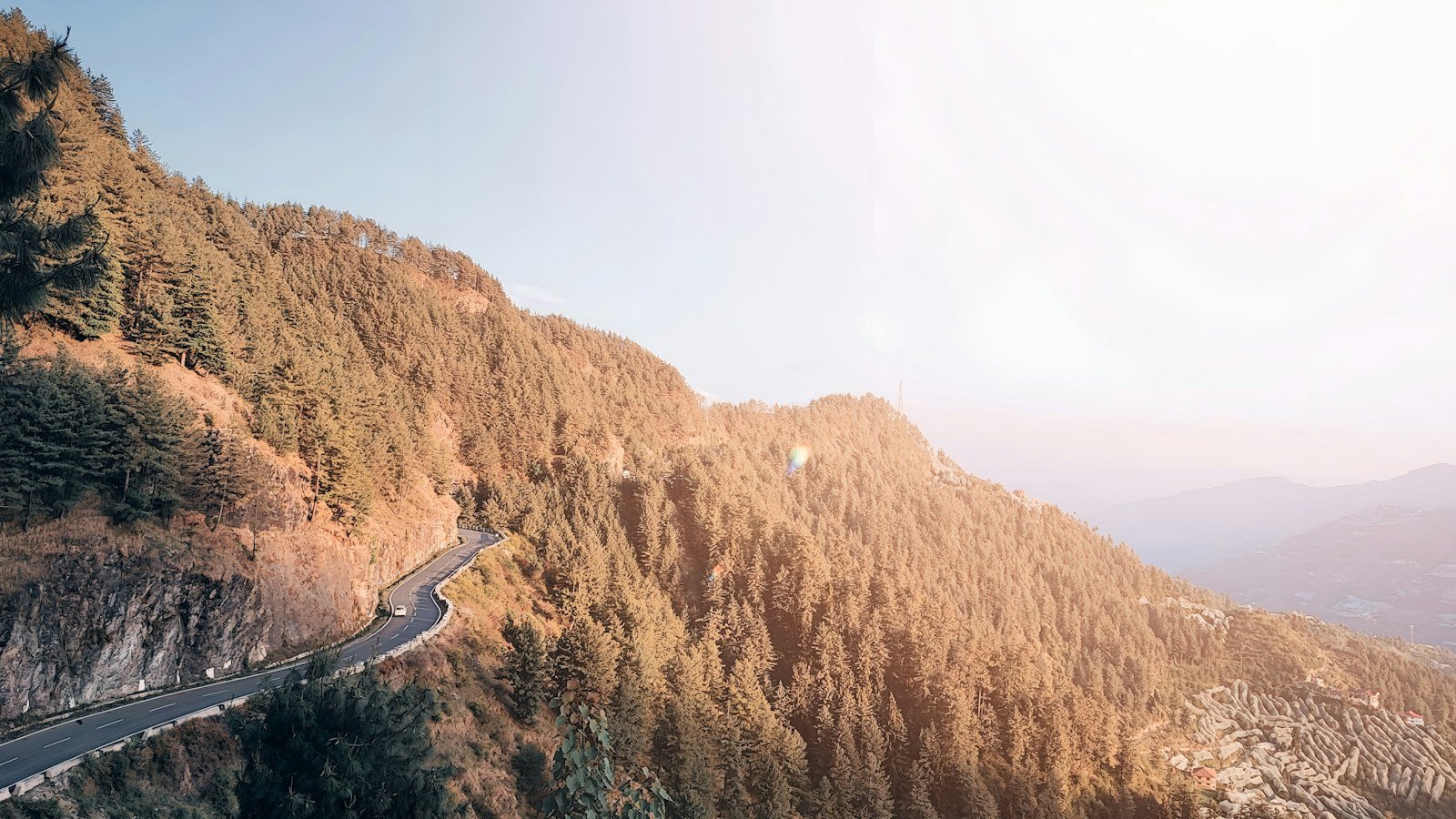 A road winding along a sunlit mountainside above a hazy valley