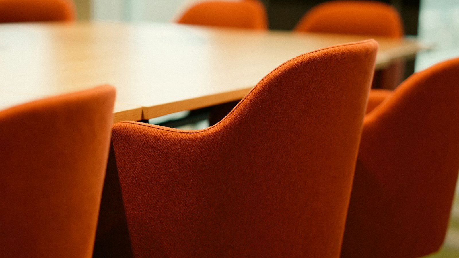 Orange chairs arranged around a wooden meeting table in an empty room