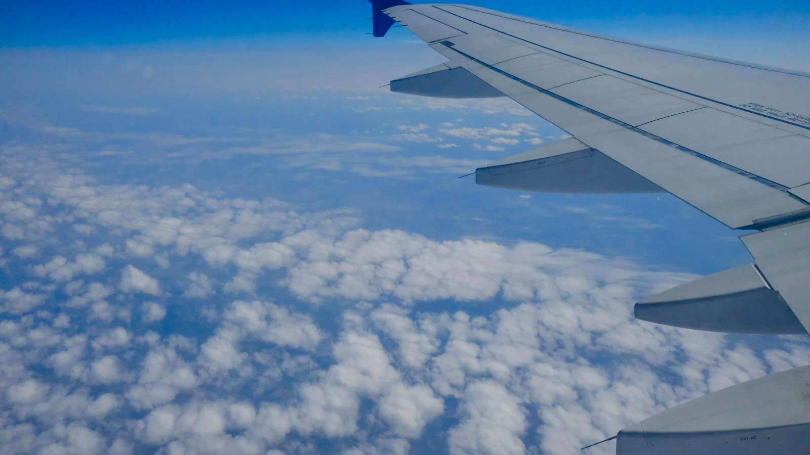 Aircraft wing above a blue sky and scattered white clouds