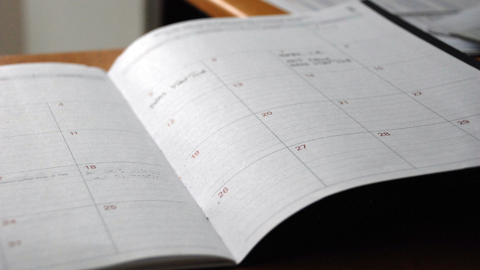 An open monthly paper planner lying on a wooden desk