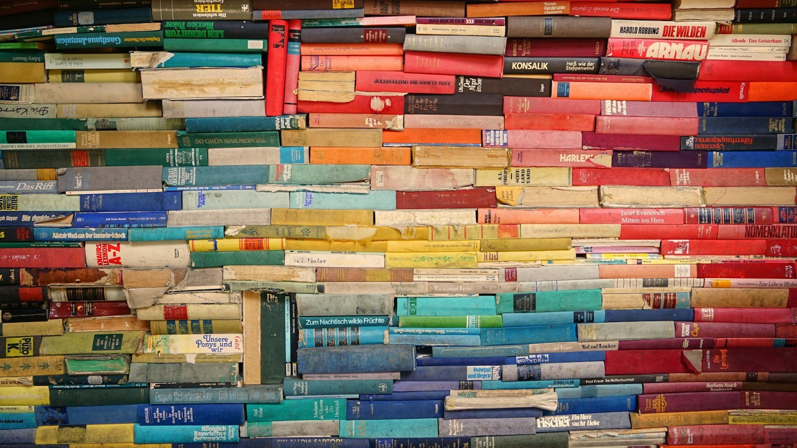 Wall of brightly coloured second hand books stacked in dense rows