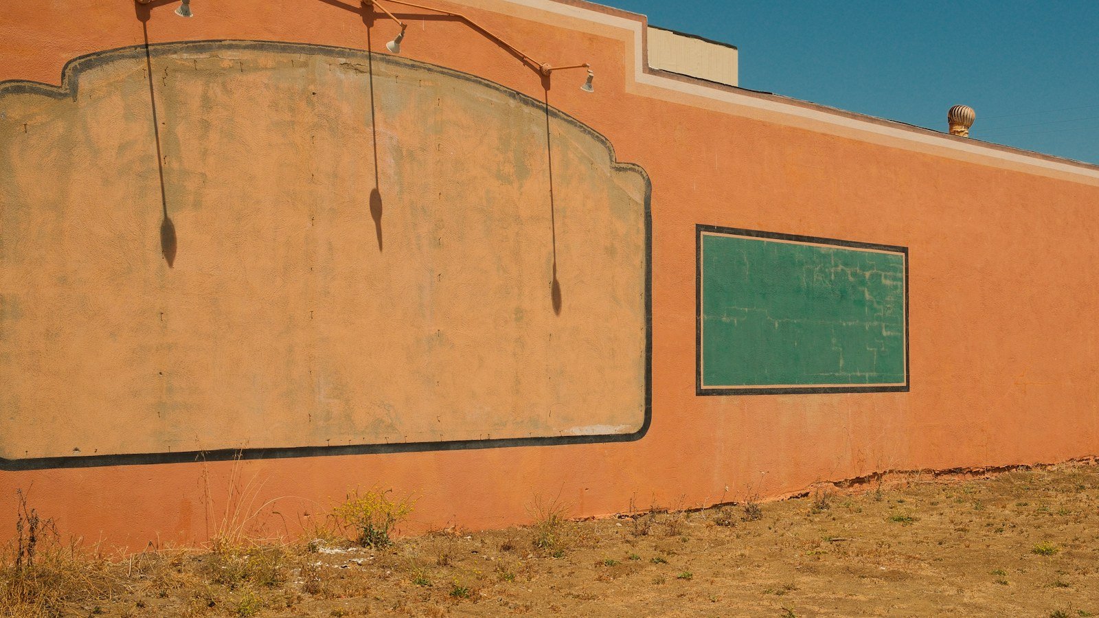Orange building wall with two blank signboards under a clear blue sky