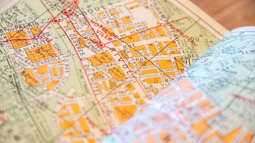 A smartphone showing a street map on a table beside a paper city map
