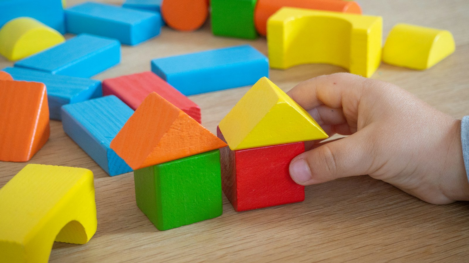 Colourful wooden toy blocks on a table with a small hand stacking one