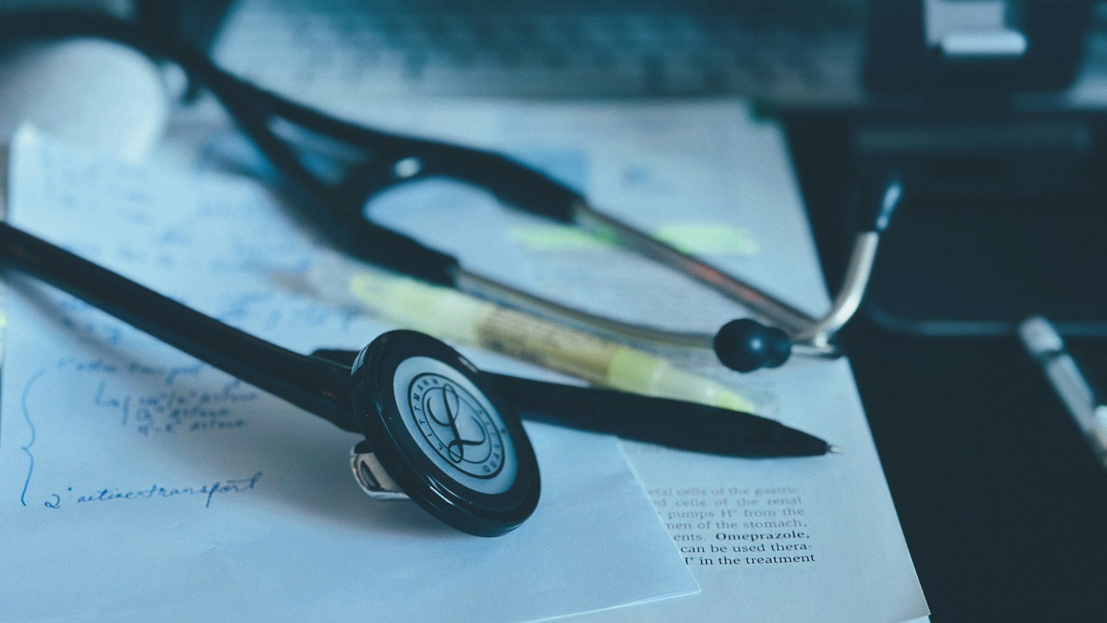 A stethoscope resting on a wooden desk beside an open notebook