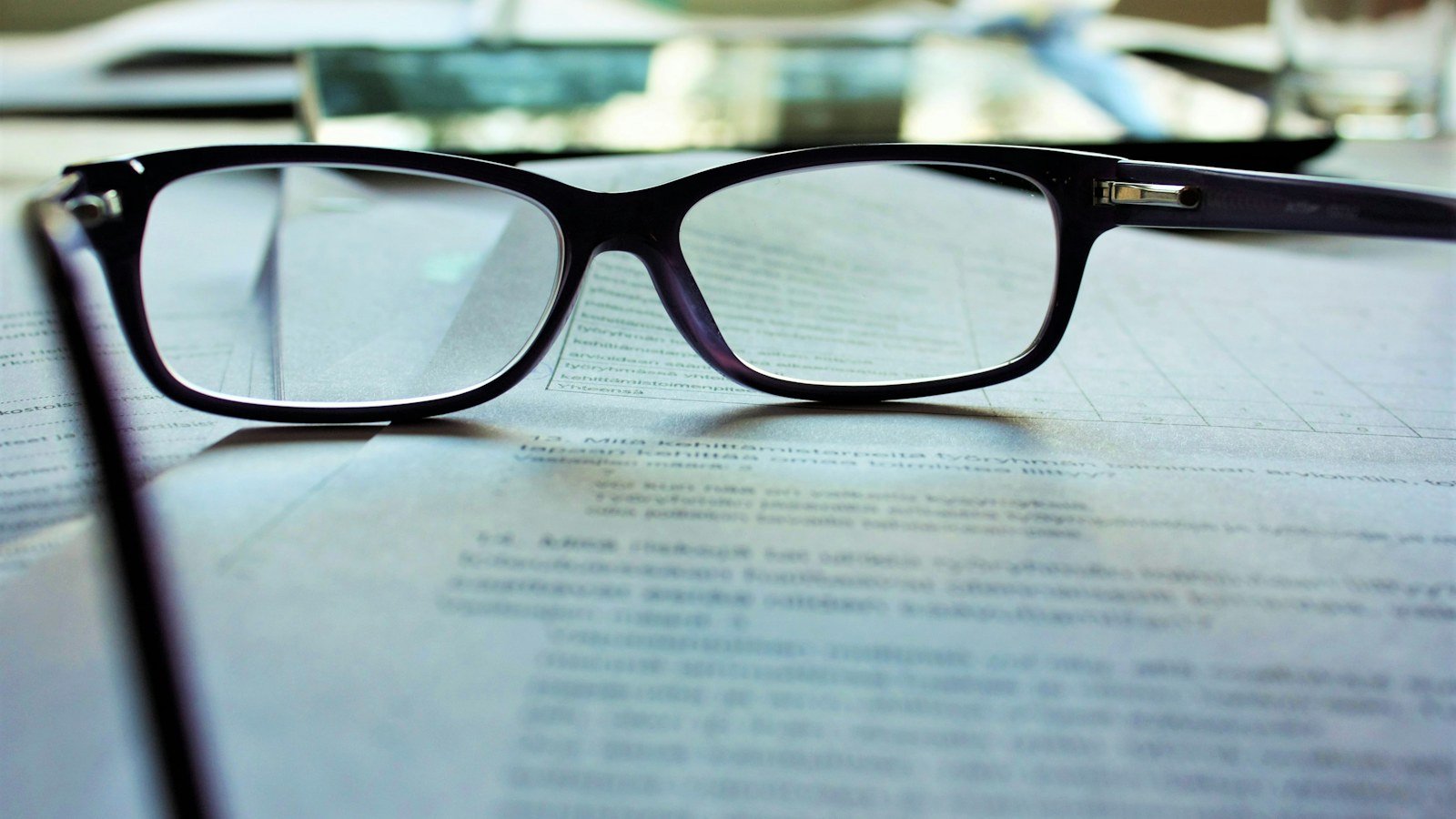 Black-framed reading glasses resting on a printed document on a desk