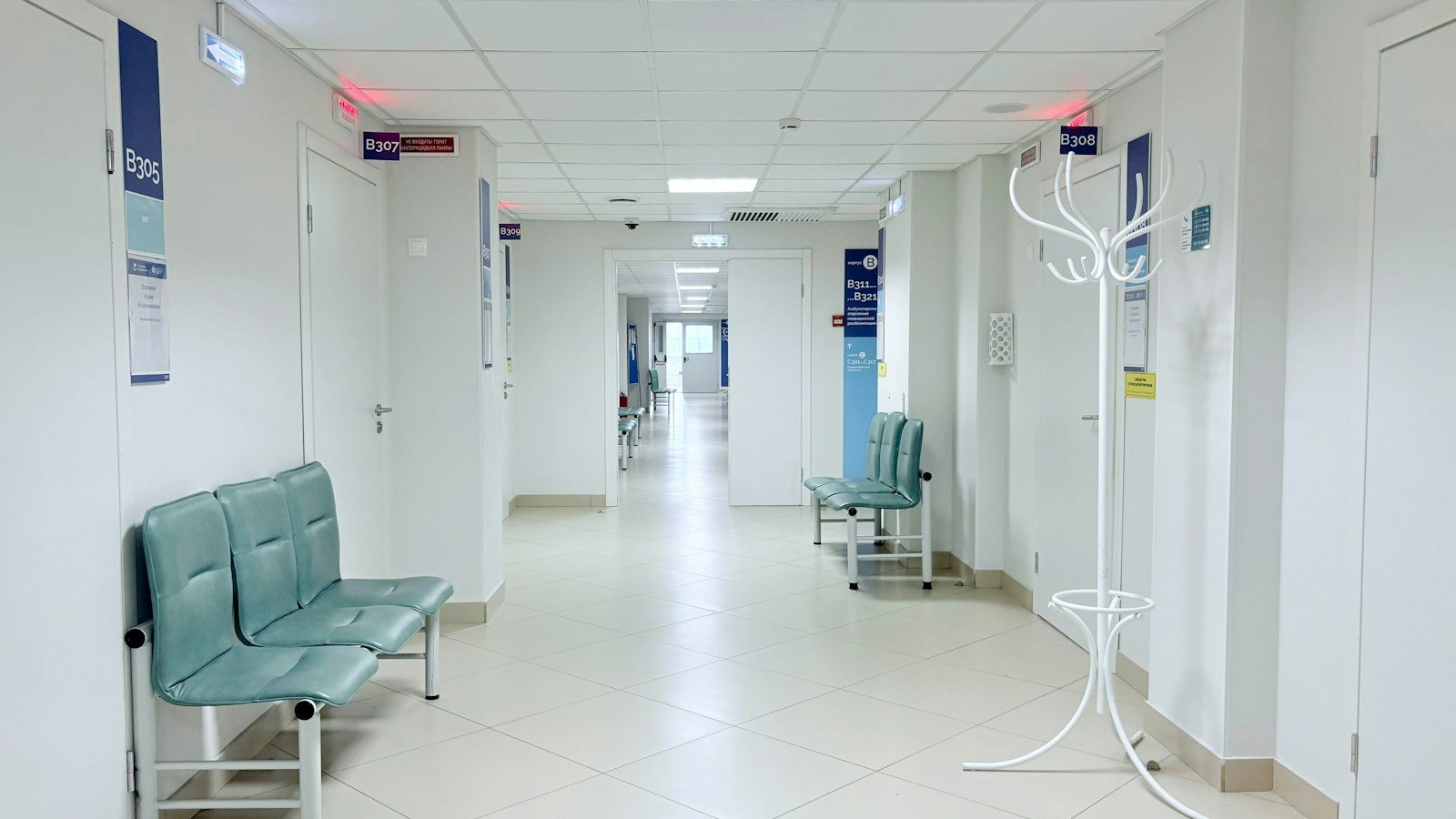 Quiet hospital corridor with teal waiting benches and closed consultation doors