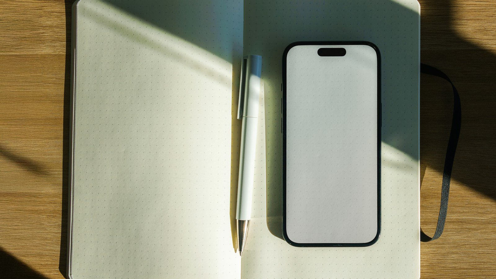 Smartphone and pen resting on an open notebook on a wooden desk