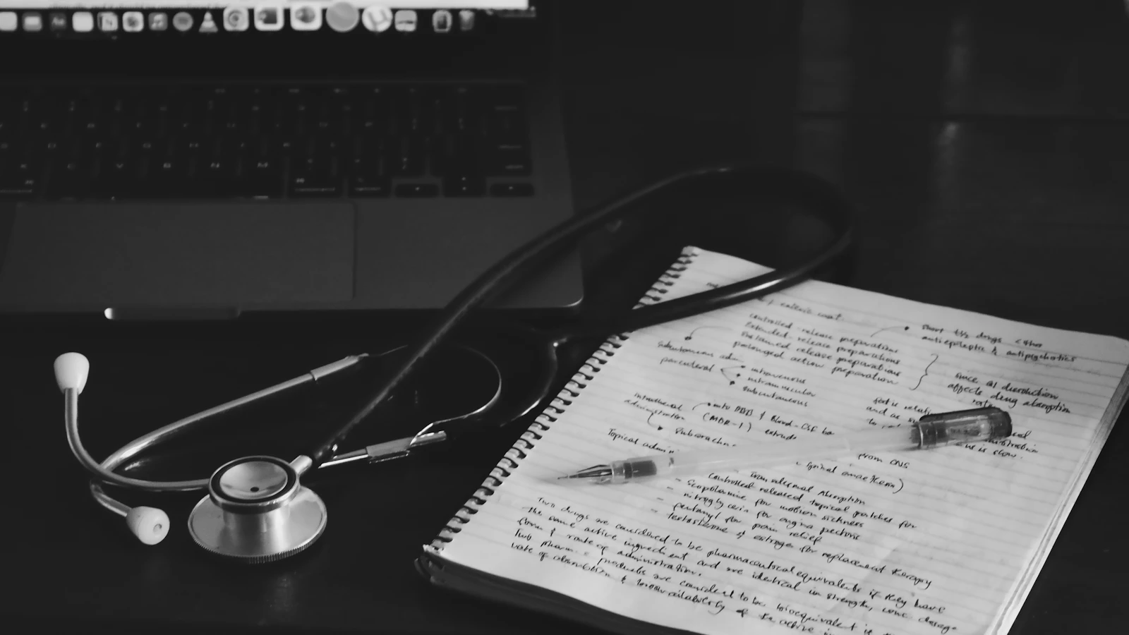 A notebook with a stethoscope on top, next to a laptop