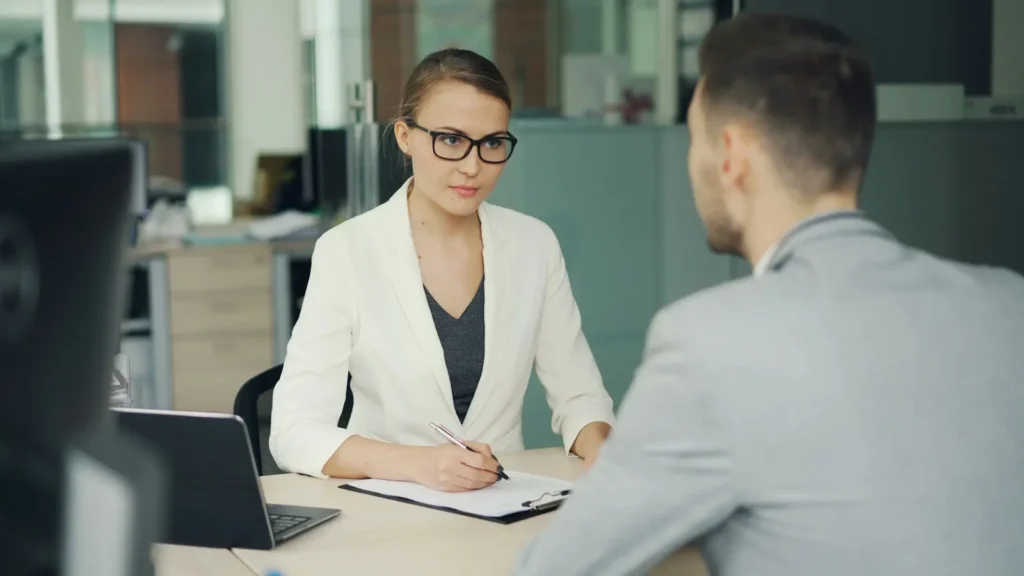 Woman in glasses interviewing a man across an office desk