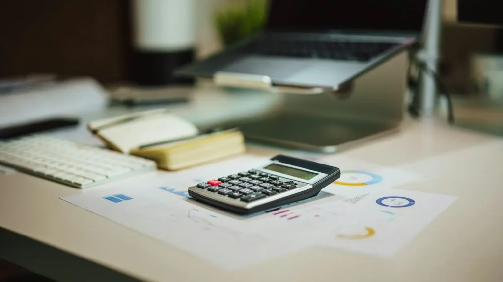 Calculator on printed charts beside a laptop on an office desk