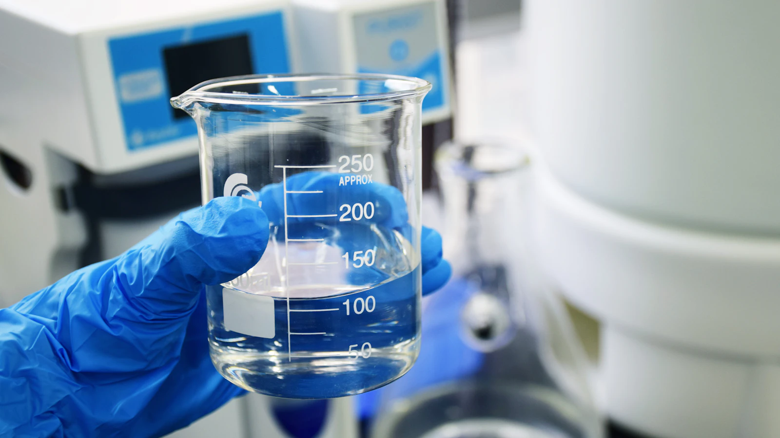 A gloved hand holding a glass beaker in a laboratory