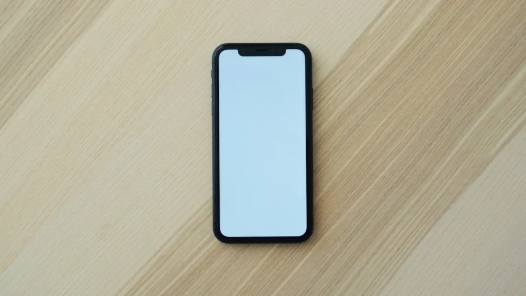 A smartphone with a blank screen lying on a pale wooden surface