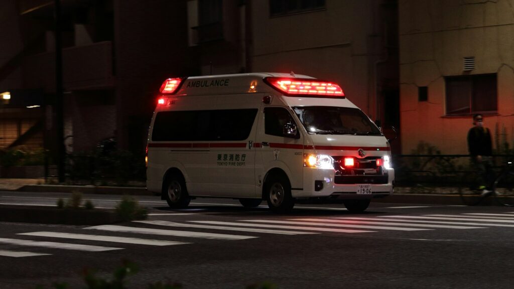 An ambulance with flashing red lights on a city street at night