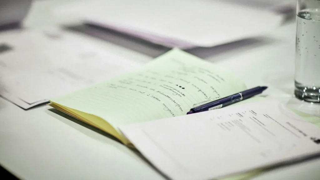 An open notepad and a pen resting on printed papers