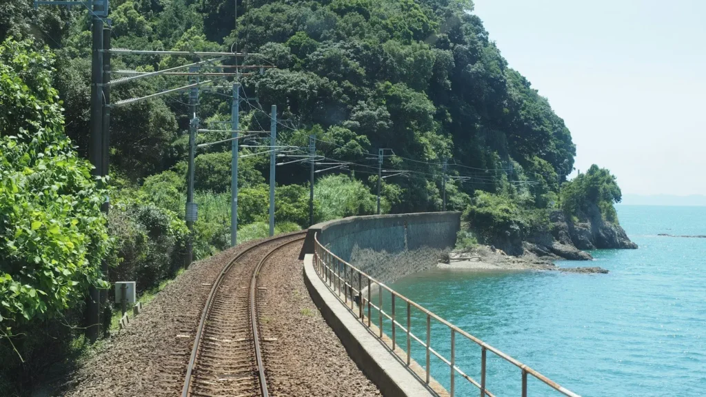 Railway track curving along a green coastline beside a blue sea