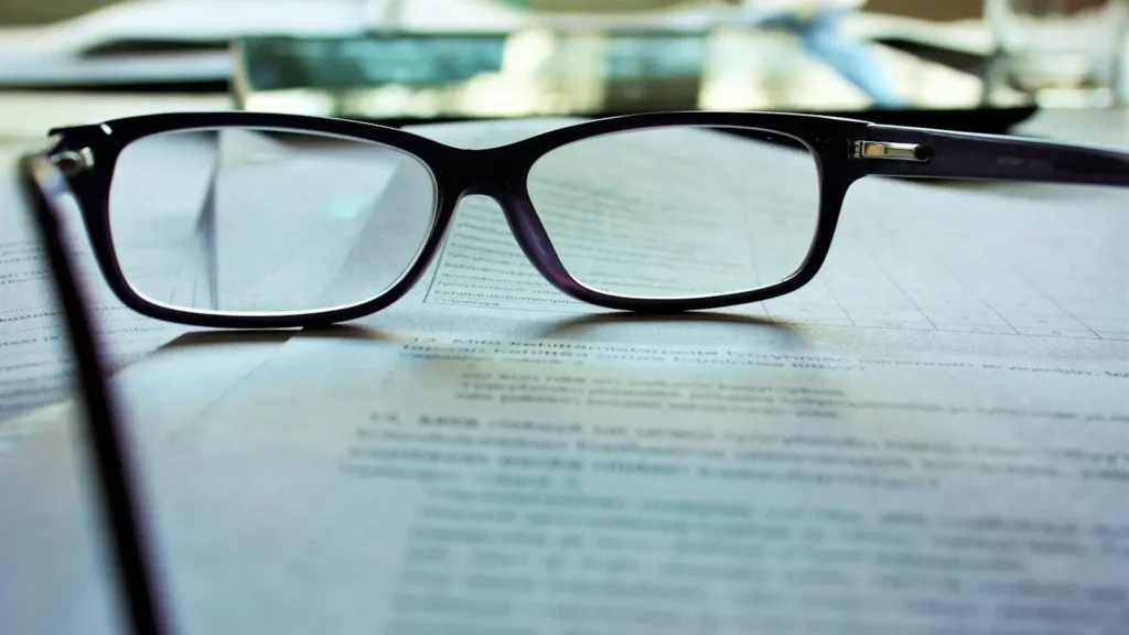 Black-framed reading glasses resting on a printed document on a desk