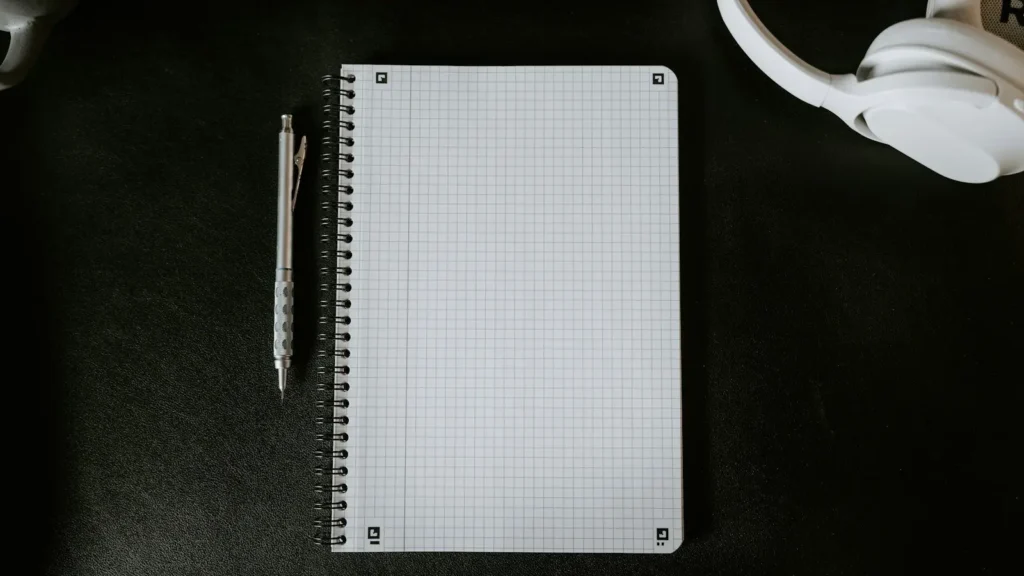 A reporter's notebook and pen beside a handheld microphone on a desk